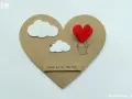 Serce z balonów w kształcie serca, unoszące się wśród chmur. Napis "Love is in the air".