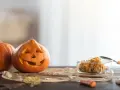 Wesoła dynia z wyciętą buzią i jej koleżanka czekają na Halloween. W szklanym naczyniu pestki dyni, gotowe na nowe pomysły na dynie.