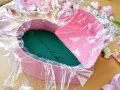 Jak zrobić flower box z winem? Różowe serce wyłożone folią i gąbką florystyczną, otoczone sztucznymi kwiatami.