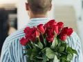 Mężczyzna z bukietem czerwonych róż za plecami. 15 roz co oznacza? Miłość, namiętność, romantyzm.