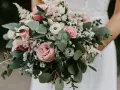 Bukiet ślubny w stylu boho: różowe róże, białe kwiaty i zielone liście eukaliptusa tworzą romantyczną kompozycję.