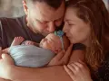 Rodzice całują śpiące maleństwo. Serdeczne gratulacje z okazji narodzin córeczki!