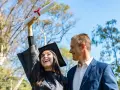 Radosna absolwentka w czapce i todze trzyma dyplom, a obok niej uśmiechnięty mężczyzna. To piękne przykładowe gratulacje z okazji ukończenia studiów.
