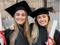 Dwie uśmiechnięte absolwentki medycyny w togach i biretach trzymają dyplomy. Gratulacje z okazji ukończenia studiów medycznych!