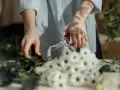 Dzień florysty. Dłonie przycinają zielone gałązki, obok bukiet białych kwiatów.