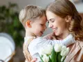 Uśmiechnięta mama i synek przytulają się, trzymając bukiet białych tulipanów. Idealny obrazek na Dzień Mamy.