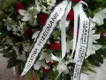 Wieniec pogrzebowy z białymi liliami i czerwonymi różami. Napis na szarfie: "Z ostatnim pożegnaniem od koleżanki i kolegów z Komendy Miejskiej Policji w Olsztynie".