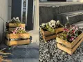 Drewniane skrzynki z kompozycjami kwiatowymi na balkon, ozdabiające wejście do domu.