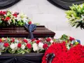 Bogata dekoracja kwiatowa, w tym róże i lilie, otacza trumnę. To piękny, pojedynczy kwiat na pogrzeb, symbolizujący pamięć i szacunek.