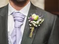Elegancki pan młody z lawendowym krawatem i bukiecikiem kwiatów do butonierki, ozdobionym białymi drobinkami i fioletowym akcentem.