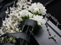 Białe kwiaty, czarna wstęga i różaniec na czarnej tkaninie. Symboliczne kwiaty na pogrzebie kolegi.