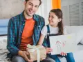 Radosny dzień ojca w Niemczech. Córka wręcza tacie prezent i rysunek przedstawiający ich rodzinę.