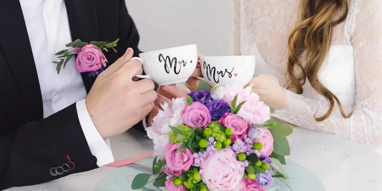 Para świętuje 4 rocznicę ślubu, trzymając kubki "Mr." i "Mrs." na tle bukietu kwiatów.