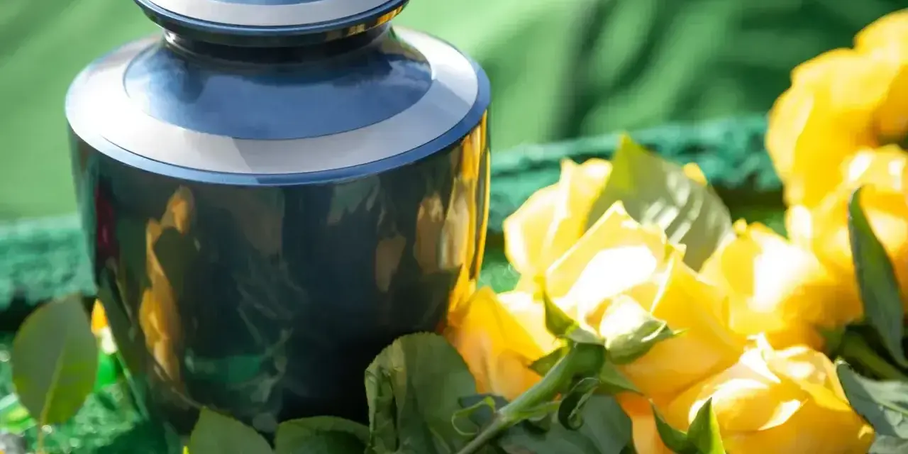 Niebieska urna pogrzebowa obok bukietu żółtych róż, kwiatów symbolizujących śmierć i pożegnanie.