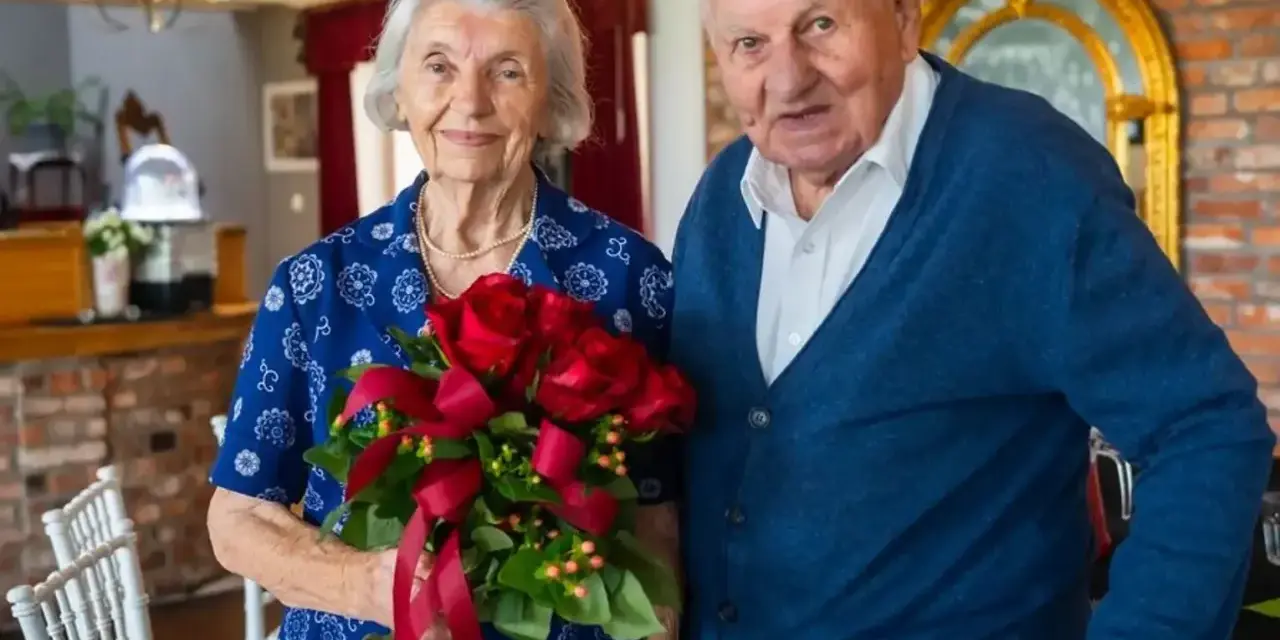 Para świętuje 70 rocznicę ślubu. Ona trzyma bukiet czerwonych róż, on stoi obok.
