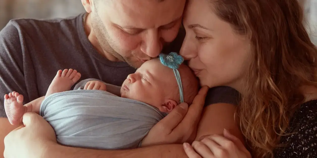 Rodzice całują śpiące maleństwo. Serdeczne gratulacje z okazji narodzin córeczki!