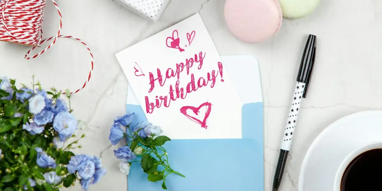 Szybkie życzenia urodzinowe: kartka z napisem "Happy birthday!", niebieska koperta, kwiaty, kawa i prezent.