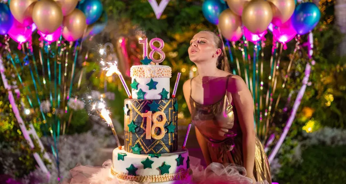 Dziewczyna zdmuchuje świeczki na torcie z okazji 18. urodzin. Balony i fajerwerki podkreślają uroczystość.