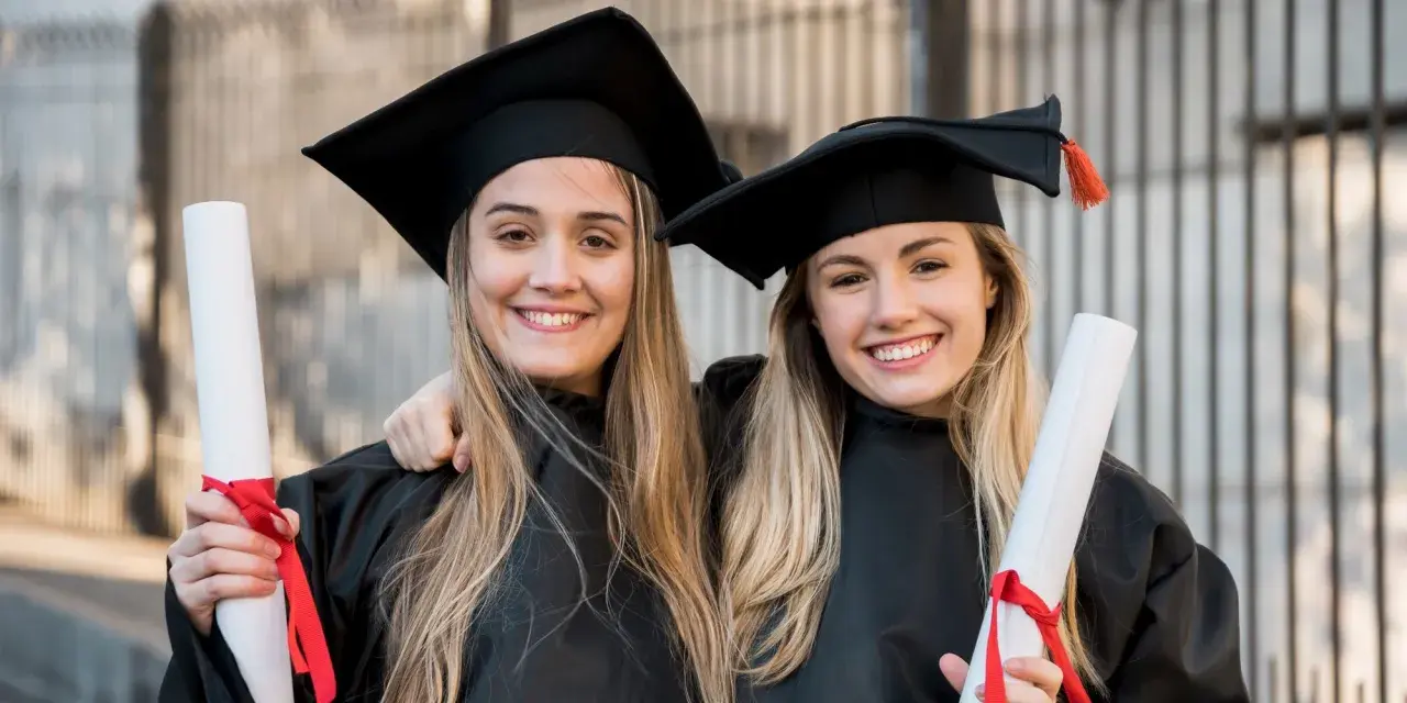 Dwie uśmiechnięte absolwentki medycyny w togach i biretach trzymają dyplomy. Gratulacje z okazji ukończenia studiów medycznych!