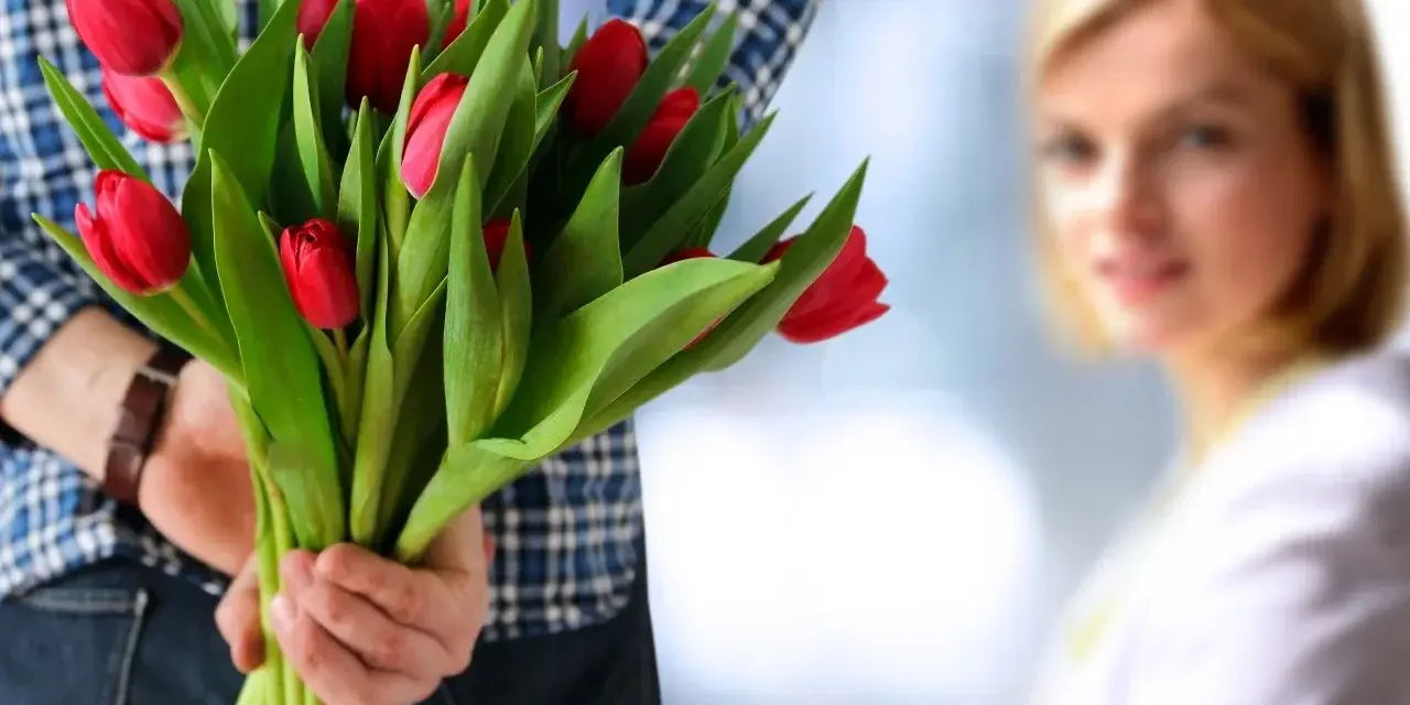 Mężczyzna z bukietem czerwonych tulipanów za plecami, zbliża się do kobiety.