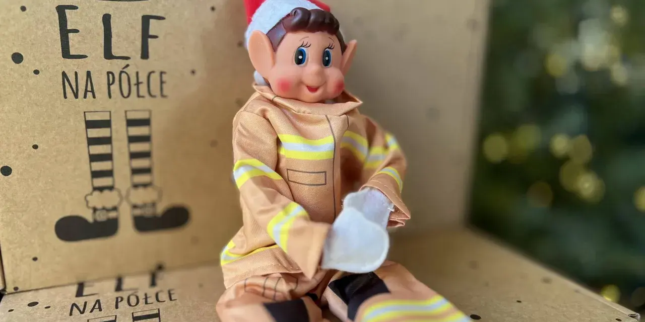 Uroczy elf na półce w stroju strażaka siedzi na kartonie z rysunkami elfich nóg.