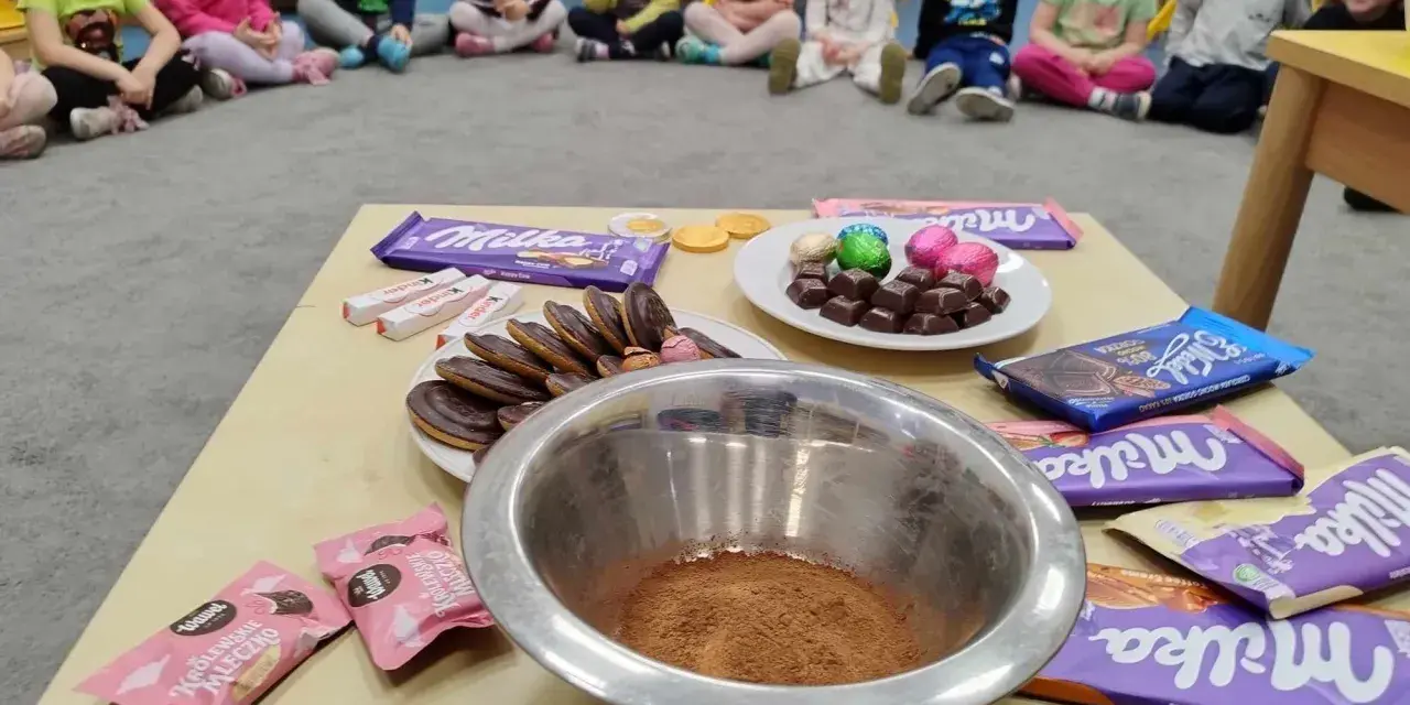 Dzieci czekają na słodkie pomysły na dzień czekolady. Na stole czekają czekolady Milka, Kinder i ciastka.