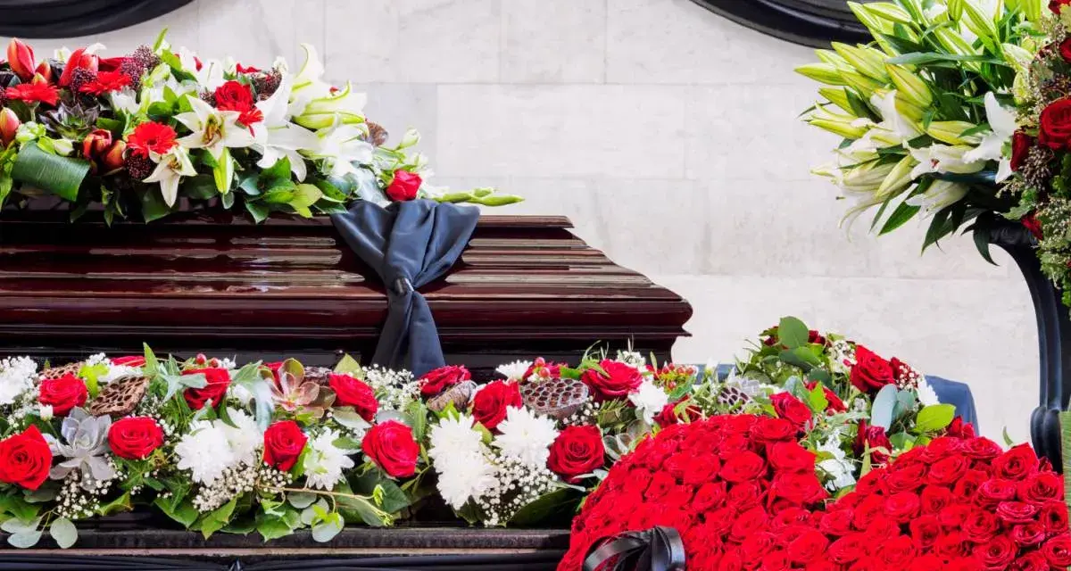 Bogata dekoracja kwiatowa, w tym róże i lilie, otacza trumnę. To piękny, pojedynczy kwiat na pogrzeb, symbolizujący pamięć i szacunek.