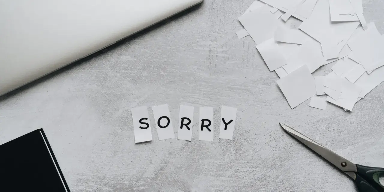 Litery wycięte z papieru układają się w napis "SORRY". Obok leżą nożyczki i stos białych skrawków, jakby ktoś tworzył piękny list na przeprosiny.