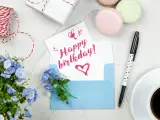 Szybkie życzenia urodzinowe: kartka z napisem "Happy birthday!", niebieska koperta, kwiaty, kawa i prezent.