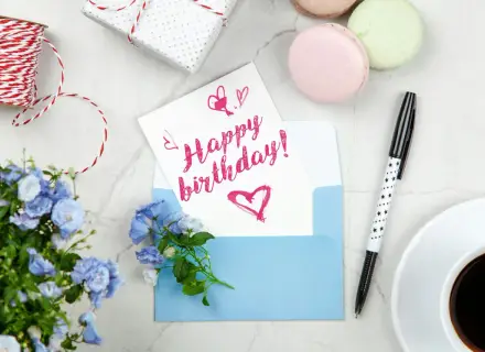 Szybkie życzenia urodzinowe: kartka z napisem "Happy birthday!", niebieska koperta, kwiaty, kawa i prezent.