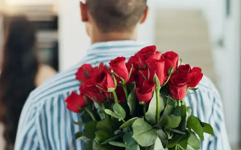 Mężczyzna z bukietem czerwonych róż za plecami. 15 roz co oznacza? Miłość, namiętność, romantyzm.