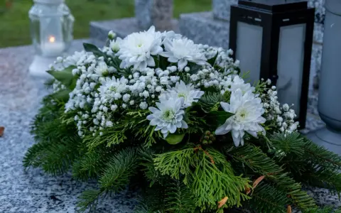 Białe kompozycje z chryzantem i iglastymi gałązkami na grobie, symbol pamięci na Wszystkich Świętych.