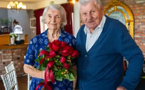 Para świętuje 70 rocznicę ślubu. Ona trzyma bukiet czerwonych róż, on stoi obok.