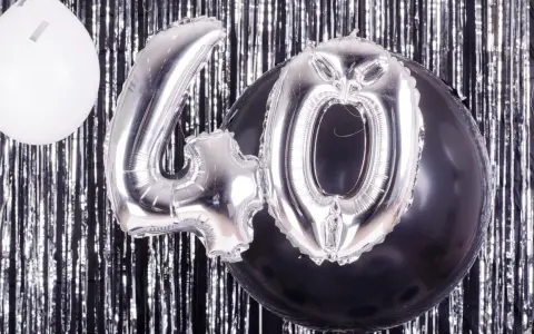 Srebrne balony z cyfrą 40 i biały balon na tle błyszczącej kurtyny. Idealne na zabawy na 40 urodziny!