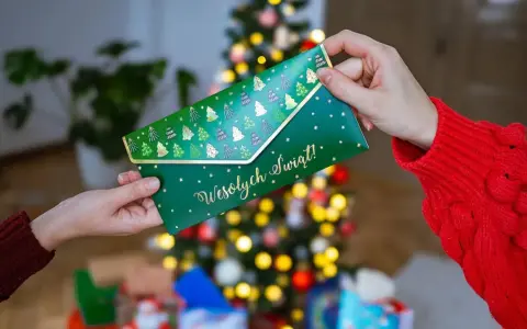 Jak zapakować voucher na prezent? Zielona koperta z choinkami i napisem "Wesołych Świąt!" jest przekazywana w świątecznej atmosferze.