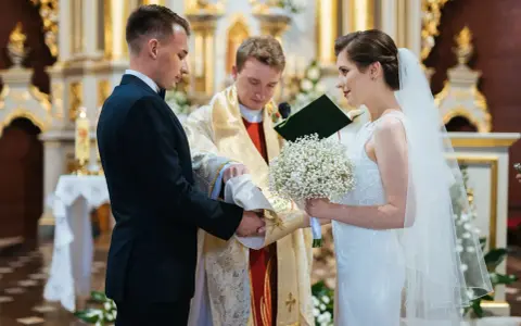 Panna młoda w welonie i z bukietem, pan młody w garniturze, podczas ceremonii ślubnej w kościele.