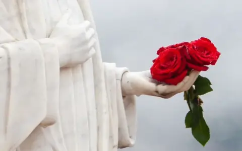 Kamienna dłoń trzyma bukiet trzech czerwonych róż.