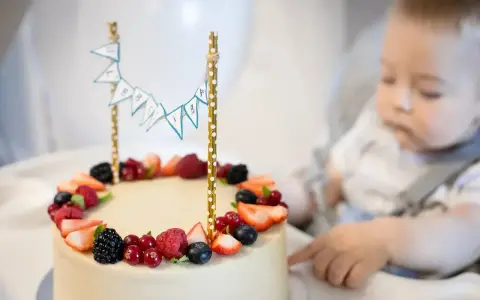 Słodki tort z owocami na przyjęcie dla dzieci. Maluch z zaciekawieniem patrzy na pyszny deser.