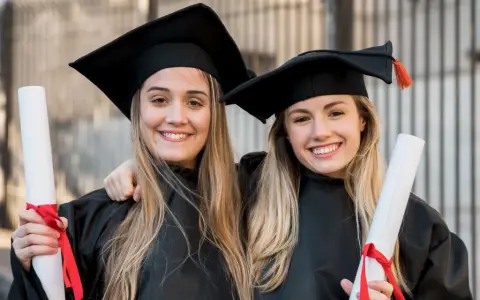 Dwie uśmiechnięte absolwentki medycyny w togach i biretach trzymają dyplomy. Gratulacje z okazji ukończenia studiów medycznych!