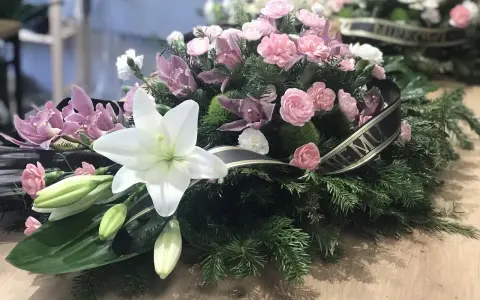 Białe lilie i różowe kwiaty w wieńcu pogrzebowym. Symbol pamięci i żalu.