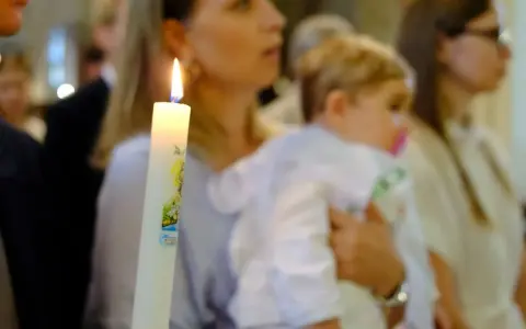 Chrzest dziecka. Czy świadek chrztu musi mieć zaświadczenie? Płonąca świeca chrzcielna w dłoniach.