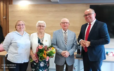 Para świętuje 65 rocznicę ślubu. Jubilaci z bukietem kwiatów, obok nich młodsza kobieta i mężczyzna w garniturze.