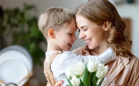 Uśmiechnięta mama i synek przytulają się, trzymając bukiet białych tulipanów. Idealny obrazek na Dzień Mamy.