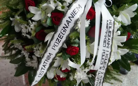 Wieniec pogrzebowy z białymi liliami i czerwonymi różami. Napis na szarfie: "Z ostatnim pożegnaniem od koleżanki i kolegów z Komendy Miejskiej Policji w Olsztynie".