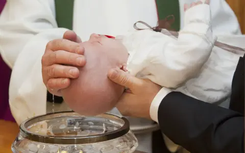 Chrzest chłopca: biała szatka, szklana chrzcielnica i woda święcona.
