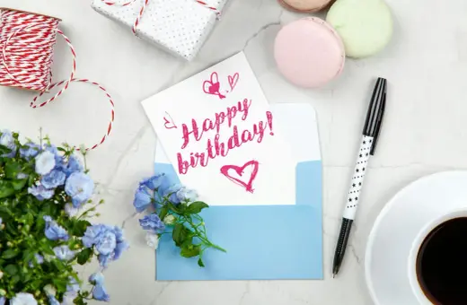 Szybkie życzenia urodzinowe: kartka z napisem "Happy birthday!", niebieska koperta, kwiaty, kawa i prezent.