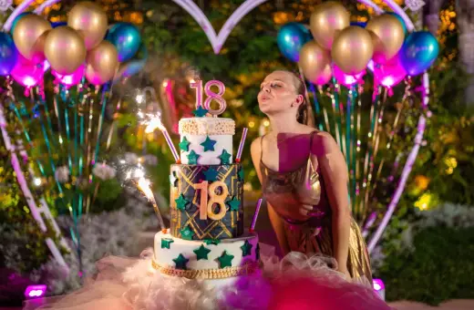 Dziewczyna zdmuchuje świeczki na torcie z okazji 18. urodzin. Balony i fajerwerki podkreślają uroczystość.