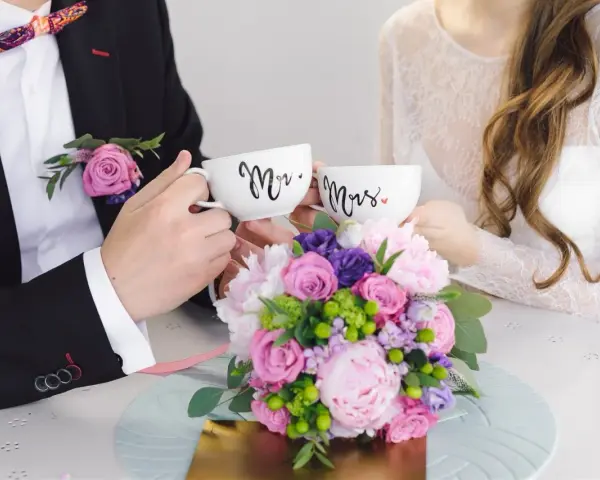 Para świętuje 4 rocznicę ślubu, trzymając kubki "Mr." i "Mrs." na tle bukietu kwiatów.