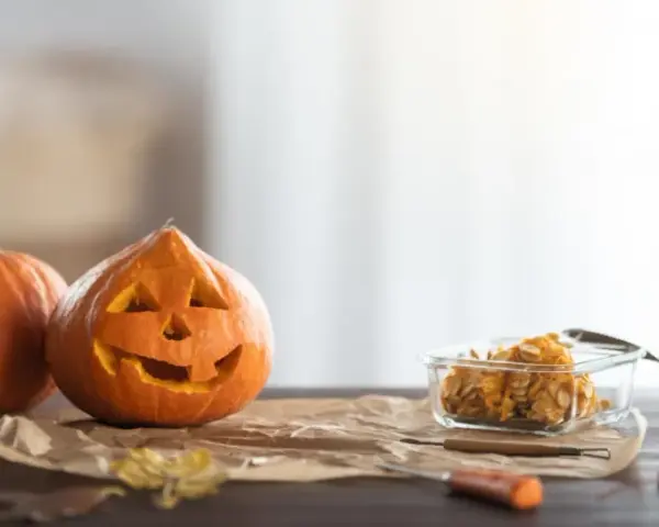 Wesoła dynia z wyciętą buzią i jej koleżanka czekają na Halloween. W szklanym naczyniu pestki dyni, gotowe na nowe pomysły na dynie.
