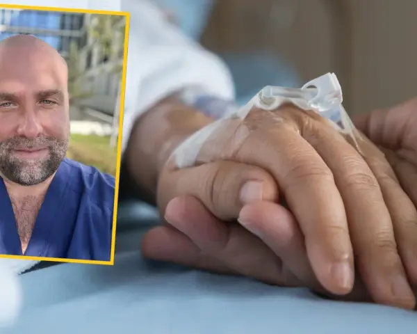 Uśmiechnięty mężczyzna w niebieskim uniformie medycznym dodaje słowa otuchy dla chorego, trzymając go za rękę.